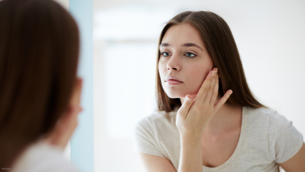 woman looking in the mirror contemplating a face lift